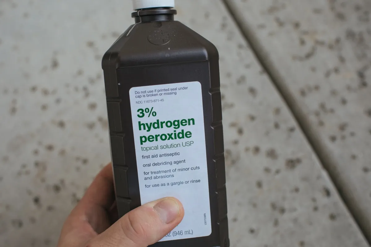 hand holding brown bottle of hydrogen peroxide on street