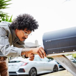 man standing outside and bending over to check for letters in his mailbox