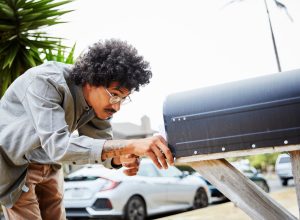 man standing outside and bending over to check for letters in his mailbox