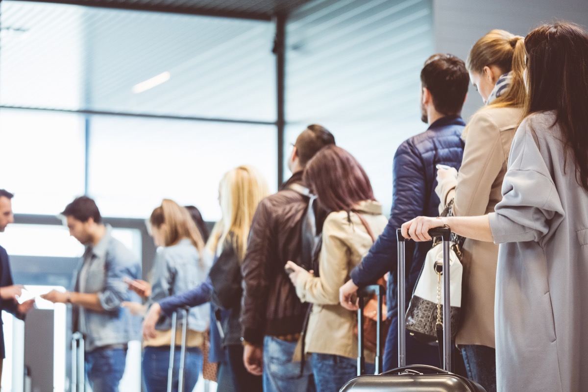 O fotografie a cozii de pasageri care așteaptă la poarta de îmbarcare din aeroport.  Un grup de oameni care stau la coadă pentru a se urca într-un avion.