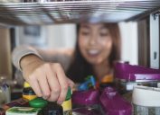 Young woman picking a bottle from storage cabinet in kitchen