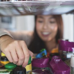 Young woman picking a bottle from storage cabinet in kitchen