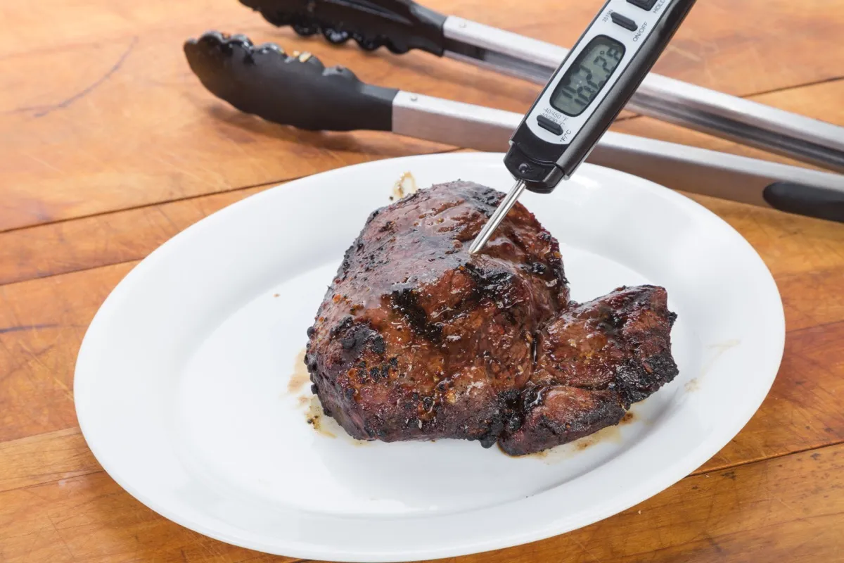 food thermometer in a piece of meat on a white plate on a wooden table