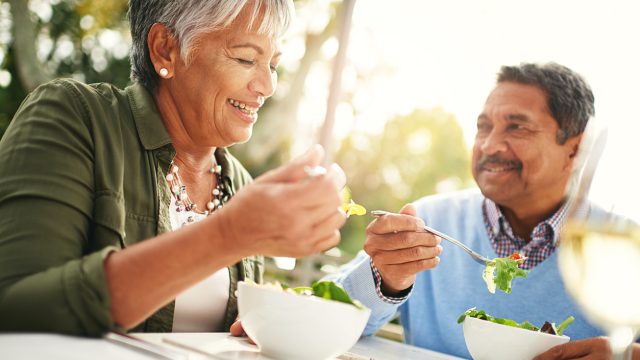 A middle-aged couple eating greens at a table outdoors