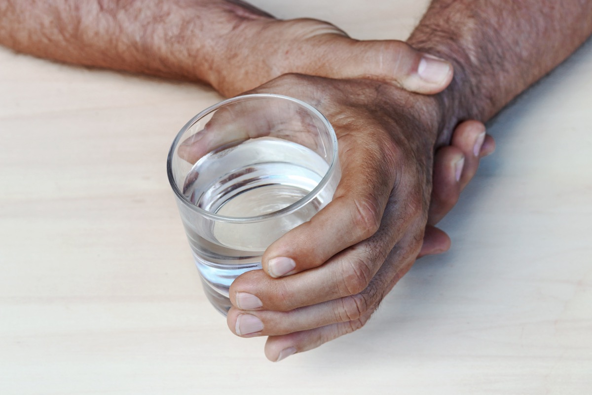older man holding wrist and a glass of water demonstrating parkinson's tremor