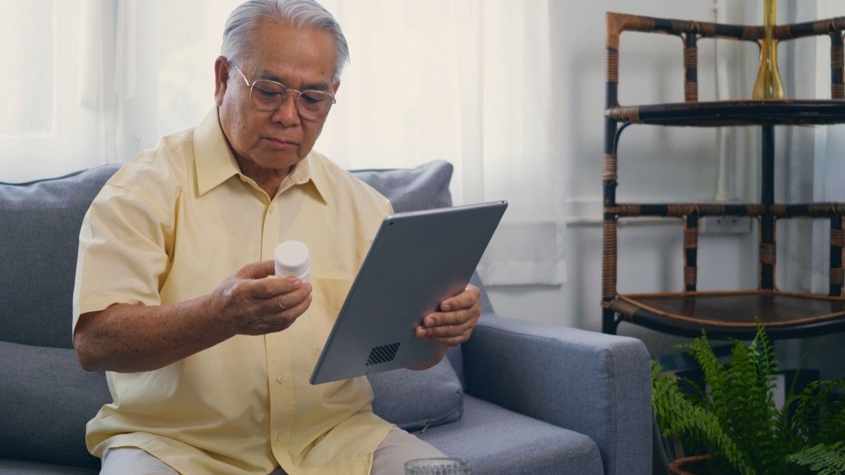 older man holding pill bottle on ipad