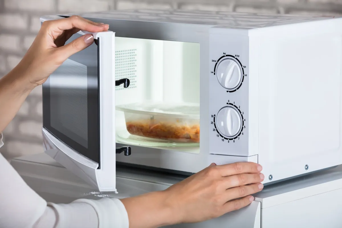 woman removing microwaveable meal from white microwave