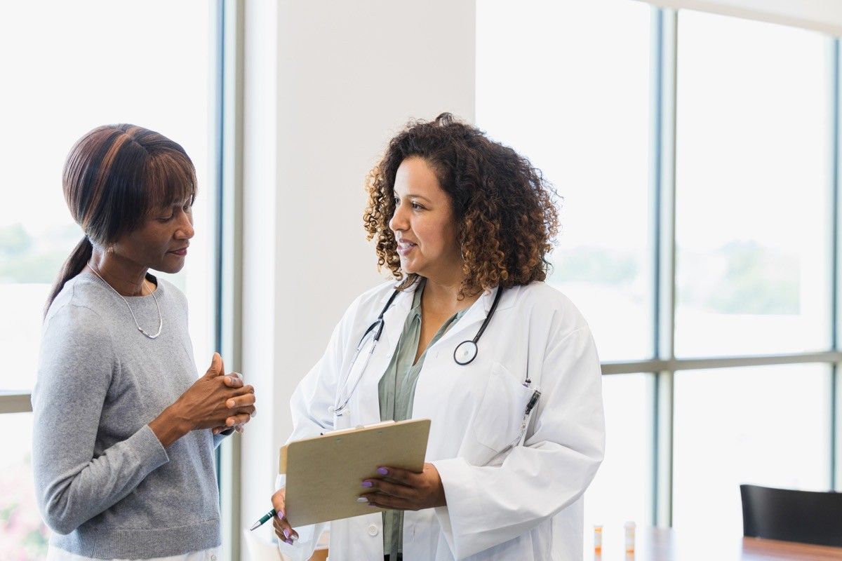 The older adult patient listens while the mid-adult doctor reviews the test results on the clipboard.