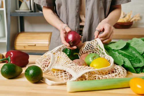 Young housewife preparing fresh vegetables for stew by kitchen table