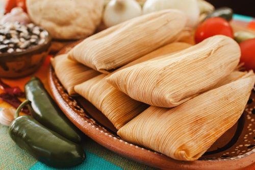 tamales wrapped in corn husks on plate next to jalapenos