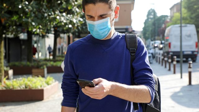 Man walking out side wearing a mask and looking at phone