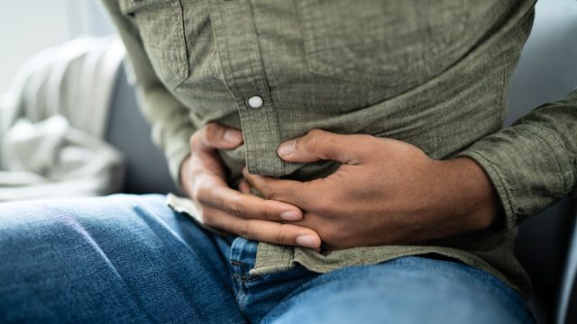 young man in jeans and green button-down with stomach pain