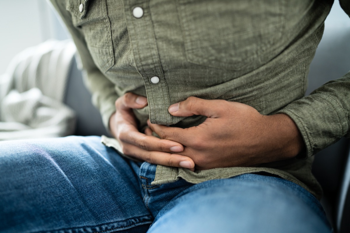 young man in jeans and green button-down with stomach pain