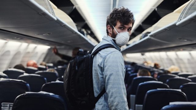 Shot of a young man wearing a mask and boarding an airplane