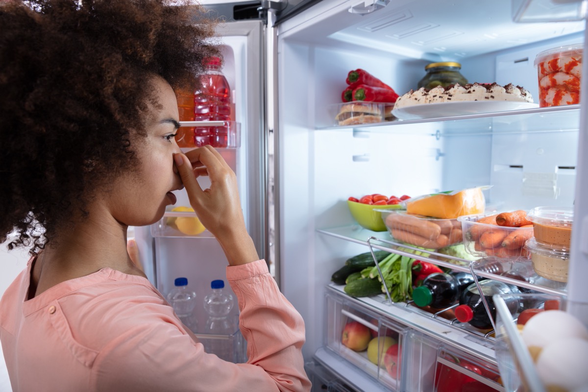 young woman looking in fridge holding nose