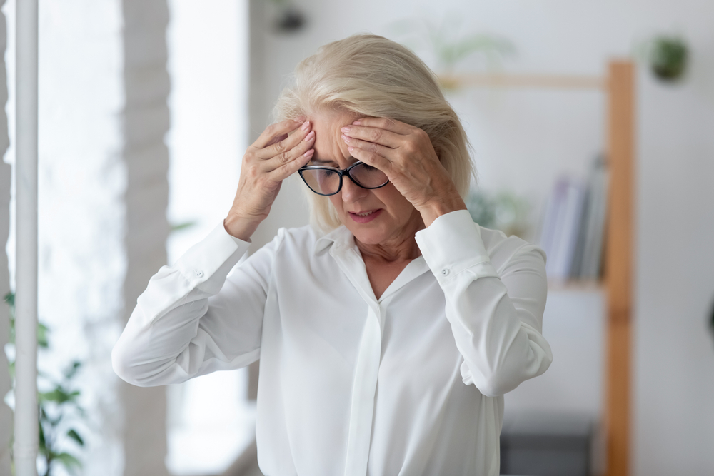 Възрастна жена се изправя и се хваща за главата от замайване или главоболие