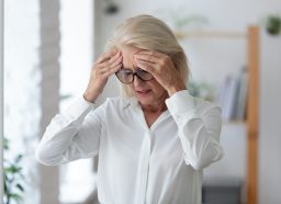 A senior woman standing up and grabbing her head from dizziness or a headache
