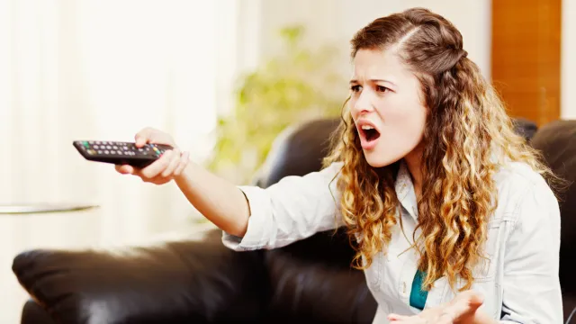 A young woman angrily pointing a remote at the TV