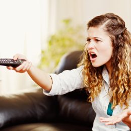 A young woman angrily pointing a remote at the TV