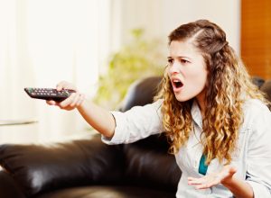 A young woman angrily pointing a remote at the TV