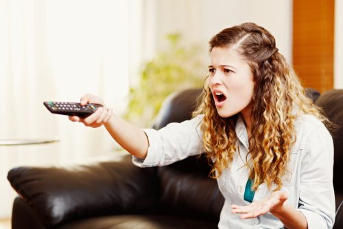 A young woman angrily pointing a remote at the TV