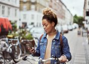 A young woman using her iPhone while riding a bike through the city