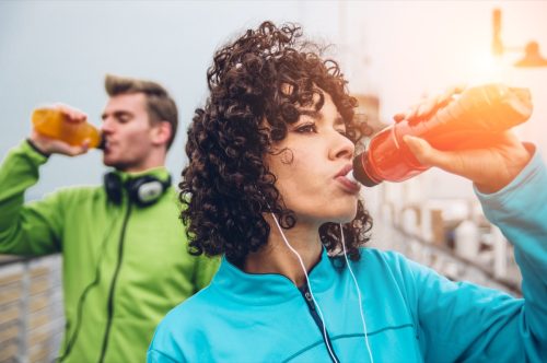 Мужчина и женщина пьют энергетический напиток из бутылки после занятий фитнесом