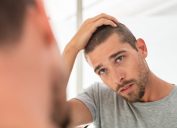 Young handsome man looking at scalp in mirror