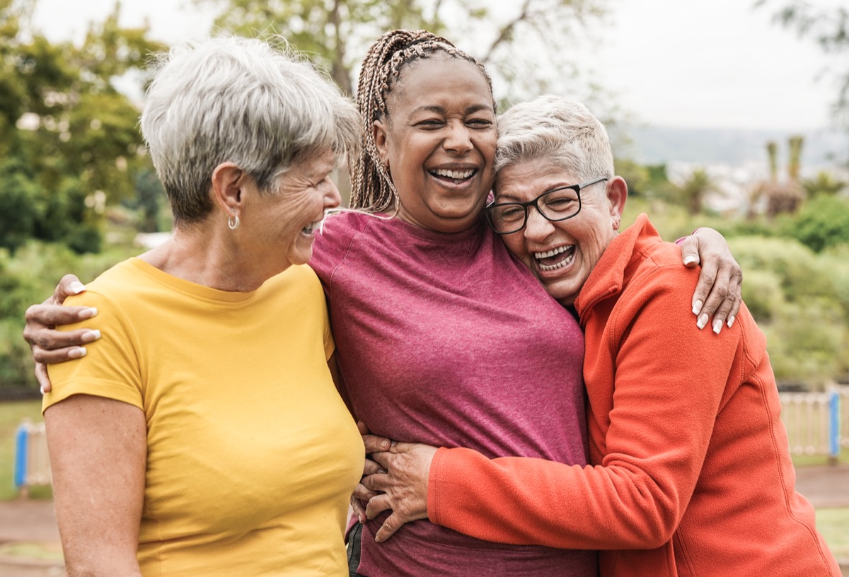 Three mature women hugging and laughing outside