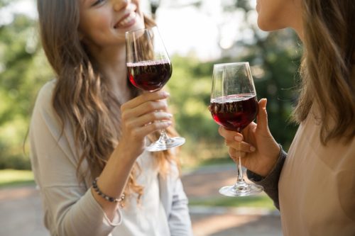 Cropped image of two young women drinking red wine outdoors