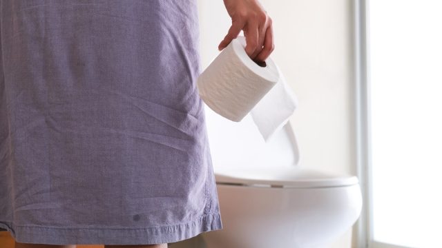 Woman holding toilet paper going into bathroom