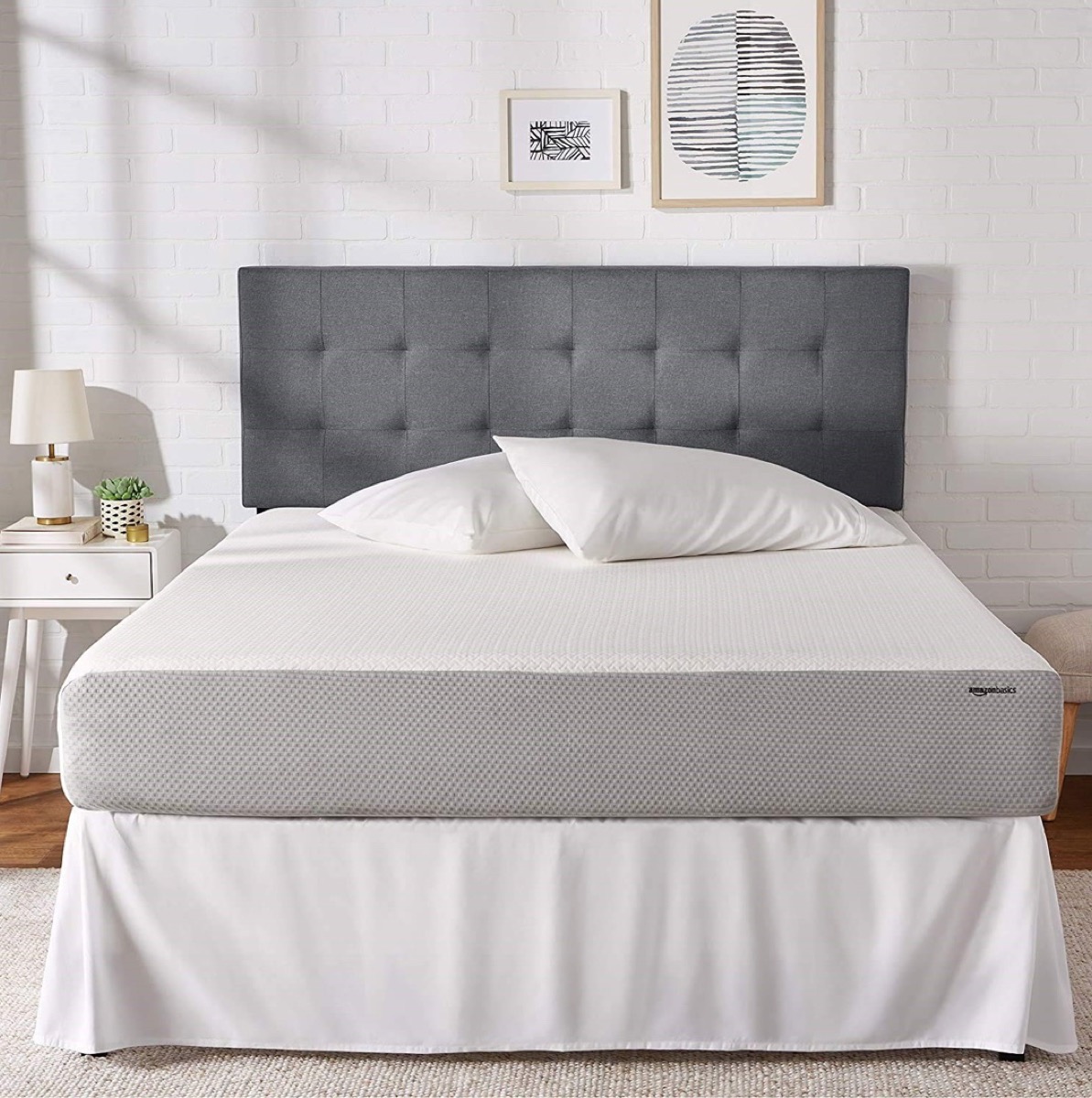 amazon basics mattress with white bedskirt against a gray headboard
