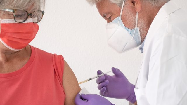 A senior woman receiving a COVID-19 booster or vaccine from a healthcare worker or doctor