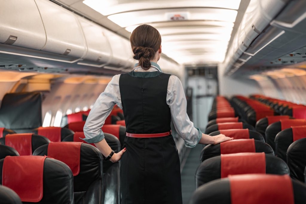 Woman flight attendant standing in aisle of empty airplane, facing away from the camera