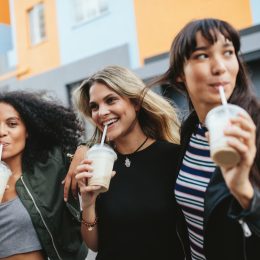 Outdoors shot of three young females having ice coffee on city street.