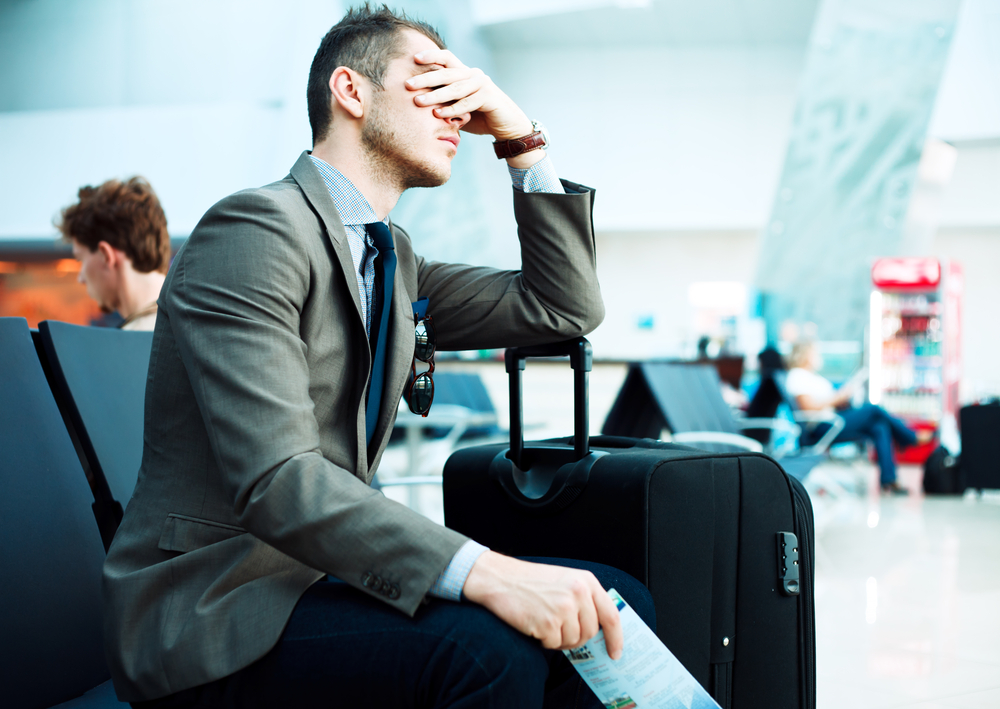 A man holding his face and angry in an airport due to a delayed flight