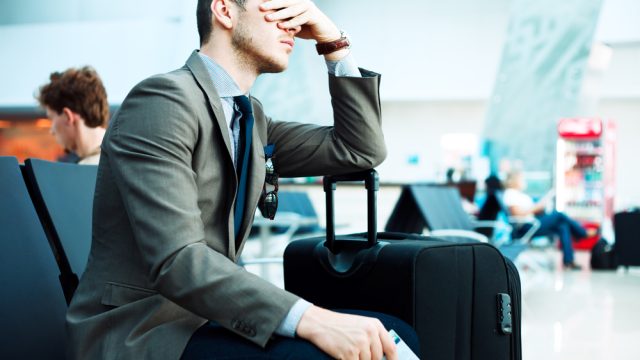 A man holding his face and angry in an airport due to a delayed flight