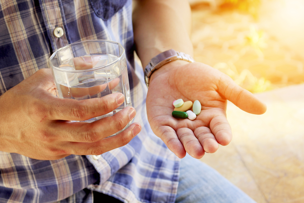 A senior man holding vitamins and supplements in this palm with a glass of water