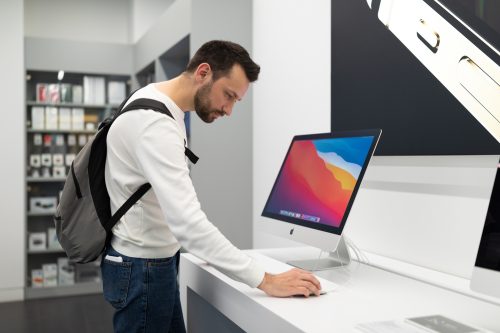 A young man wearing a backpack testing out an iMac computer in an Apple store