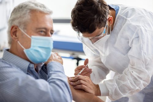 Un bărbat în vârstă care primește un vaccin COVID-19 sau o doză de rapel de la un lucrător din domeniul sănătății