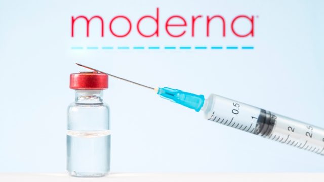 A vial of COVID-19 vaccine and a syringe in front of the Moderna logo