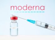 A vial of COVID-19 vaccine and a syringe in front of the Moderna logo