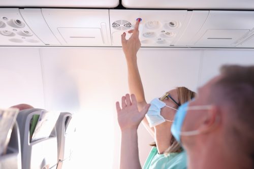 Man and a woman in protective medical masks press call button on plane. Maintenance and service during flights concept