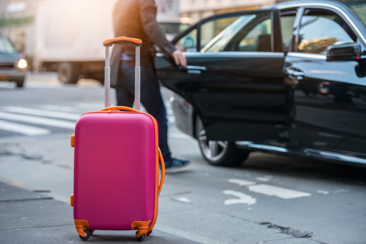 pink suitcase on sidewalk in front of black taxi cab