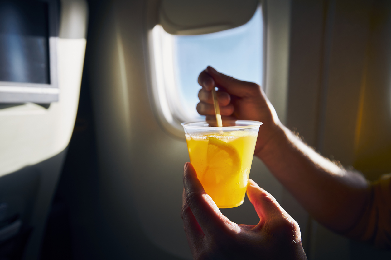 Close up of a person holding a cocktail with a plastic straw on a plane during a flight