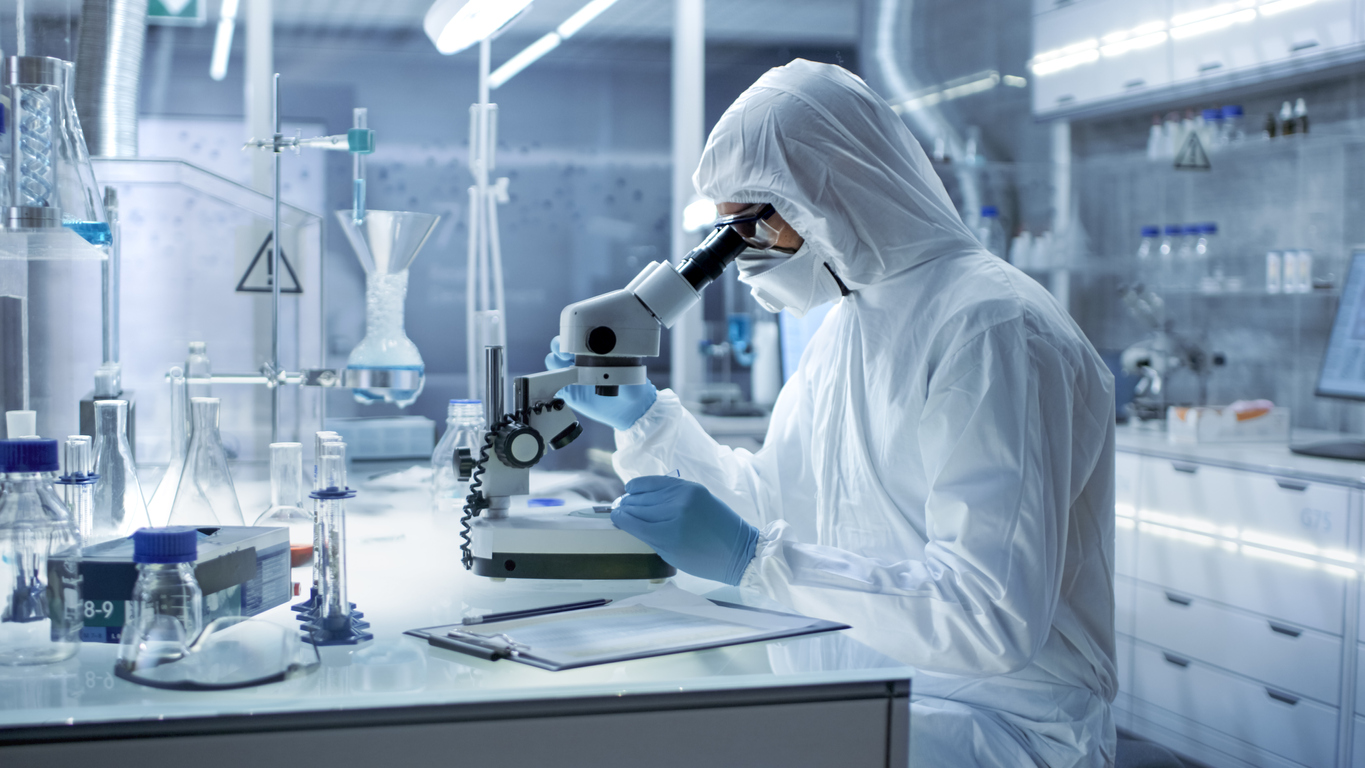 Un om de știință a terminat un studiu în laborator uitându-se într-un microscop în timp ce purta echipament de protecție complet