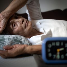 A senior woman lying awake in bed at night while looking at her alarm clock