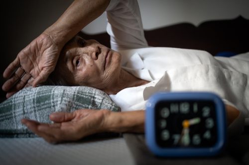 A senior woman lying awake in bed at night while looking at her alarm clock