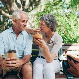 A senior couple sitting on a bench while eating a snack and drinking coffee