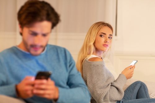 suspicious woman looking over at man texting on the couch